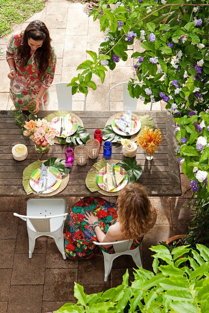 Zwei Frauen an gedecktem Gartentisch in sommerlicher Gartenfeststimmung unter blühendem Strauch