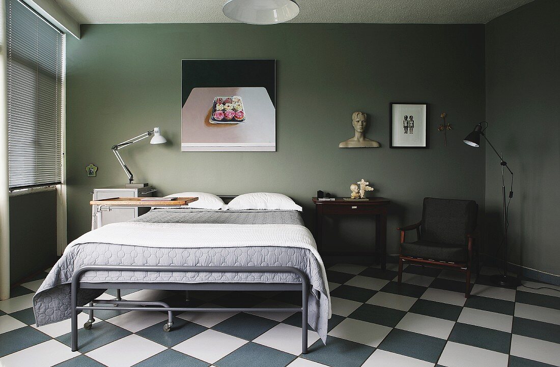Vintage-Bett mit grauem Metallgestell vor olivgrau getönter Wand mit modernem Bild in Schlafzimmer mit Schachbrettmusterboden