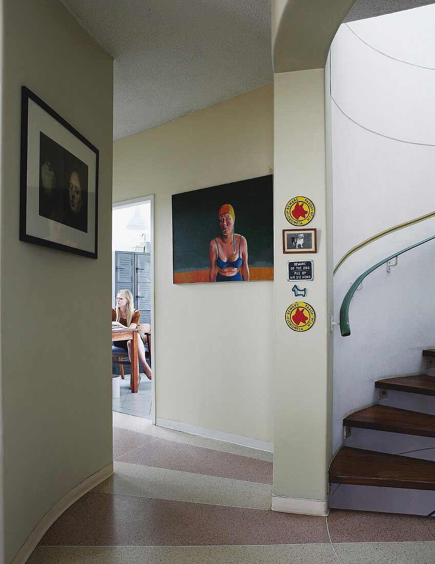 Bilder an getönter Wand im Vorraum, seitlich teilweise sichtbare Wendeltreppe, im Hintergrund offene Tür und Blick auf junge Frau