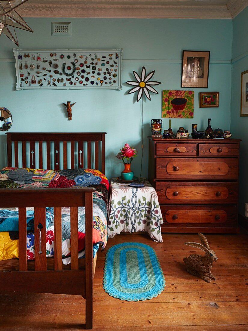 Holzbett mit Gittergestell und Nachttisch neben Schubladenkommode an türkisfarbener Wand in künstlerischem Ambiente