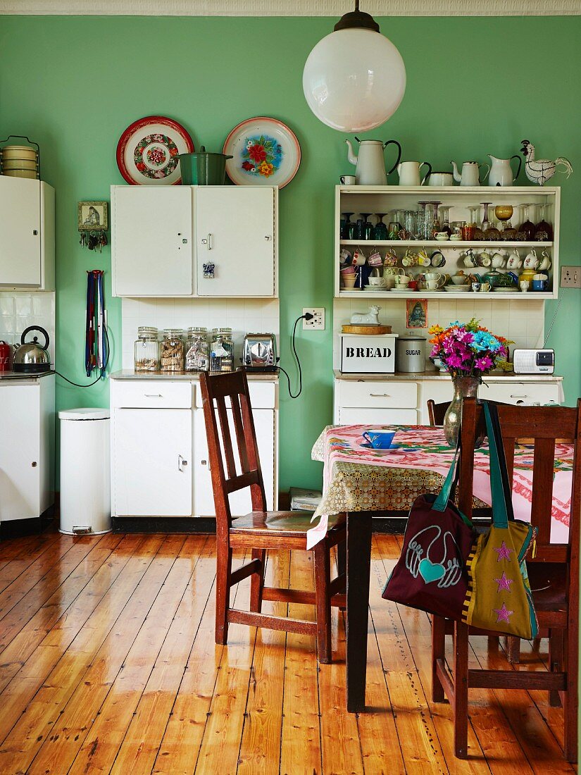 Holzstühle um Tisch auf gepflegtem Dielenboden in schlichter, funktionaler Küche, weiße Schränke an grün getönter Wand