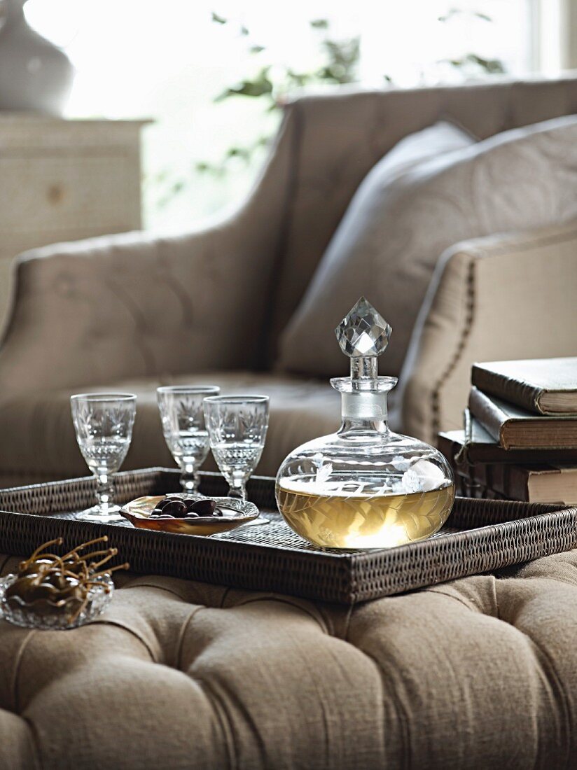 Glaskaraffe mit geschliffenen Gläsern auf Korbtablett in elegantem Ambiente auf Polstertisch serviert