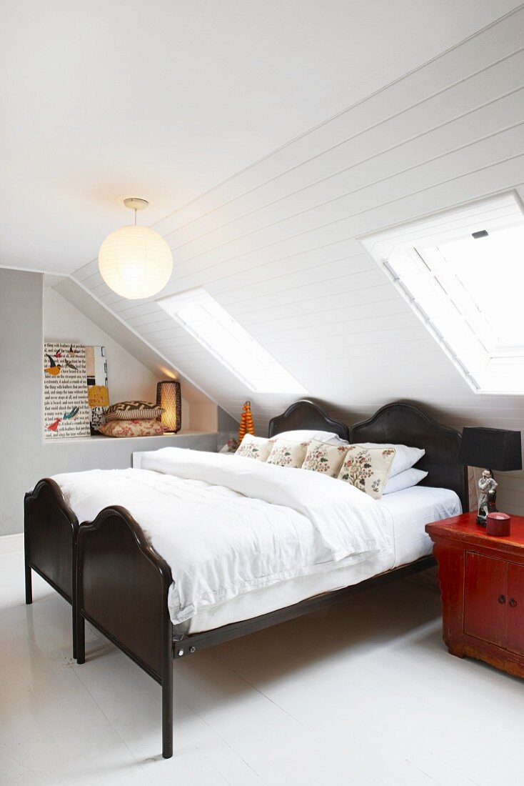 Twin beds with black wooden frames under sloping ceiling with white wood panelling