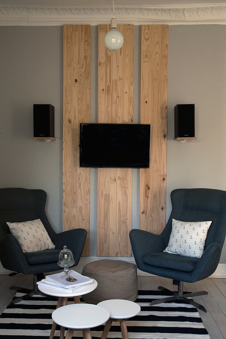 Beistelltische und Drehsessel vor Holzpaneelen mit Flatscreen und seitlich an der Wand befestigten Lautsprechern