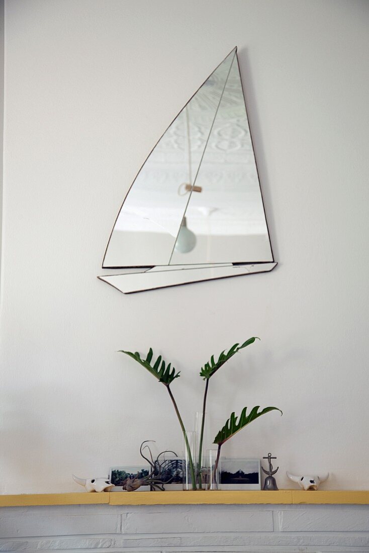Mirror in shape of sailing boat above arrangement on mantelpiece