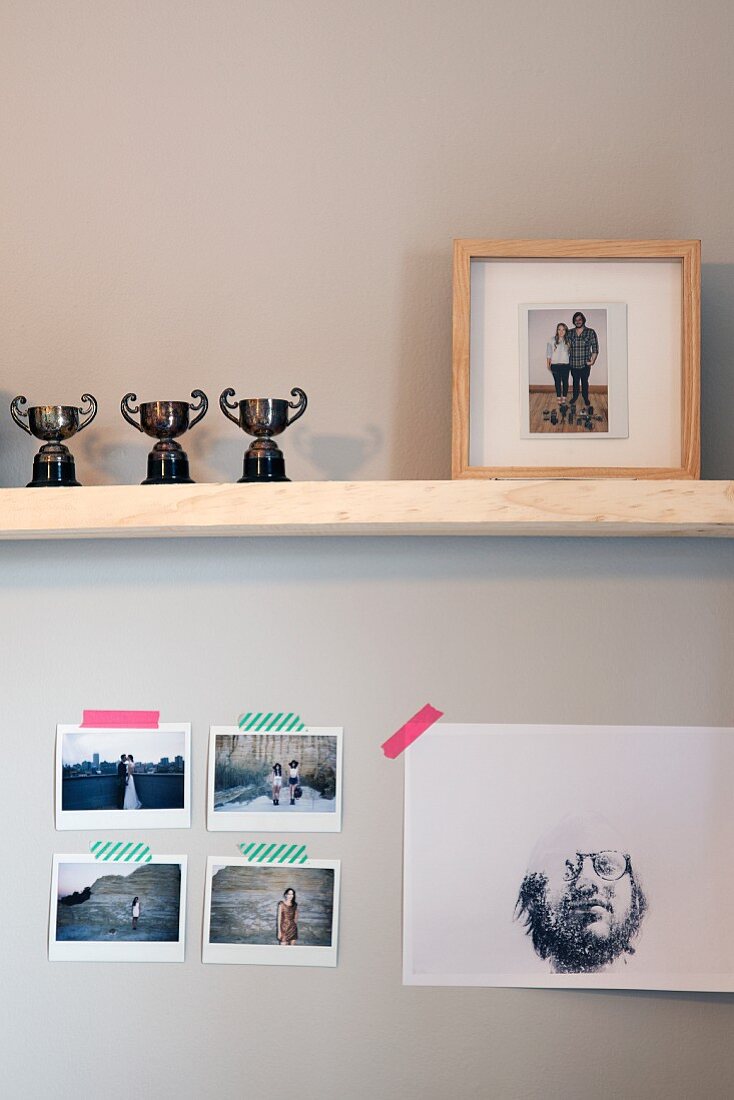 Three trophies and framed photo of couple on wooden shelf above photos attached to wall with washi tape