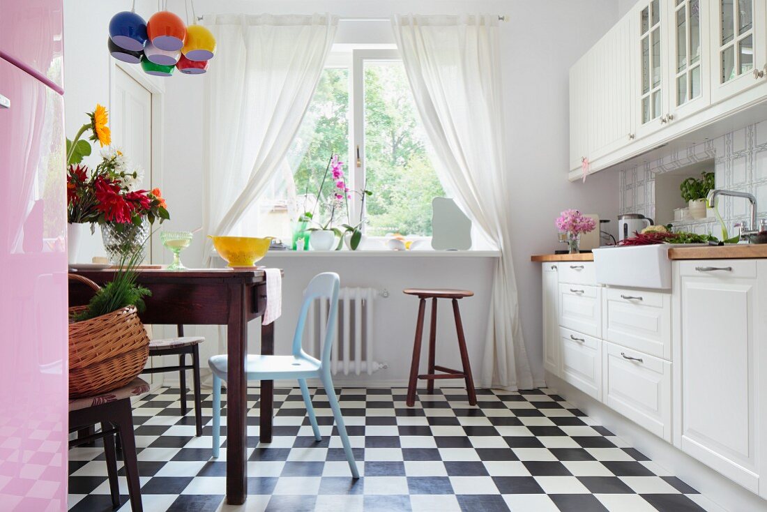 White country-house kitchen with black and white chequered floor, old wooden table in dining area and retro chairs