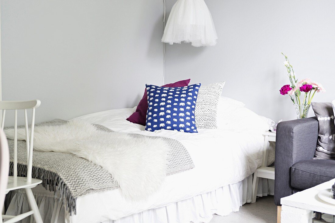Dekokissen und sorgfältig ausgewählte Decken in Schichten auf einem Bett - sanft grauweisses Ambiente mit wenigen Farbakzenten