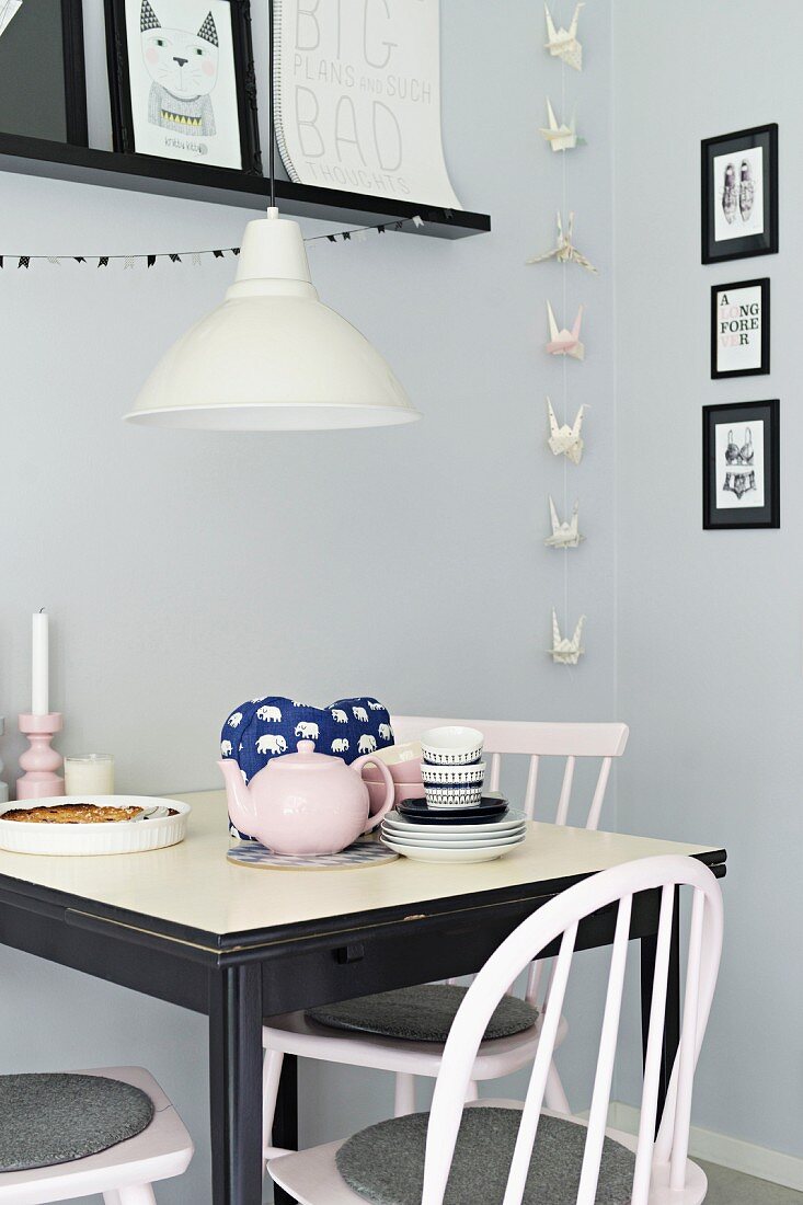 Small, black and white dining area in front of grey-painted wall with origami garland and gallery of black-framed pictures