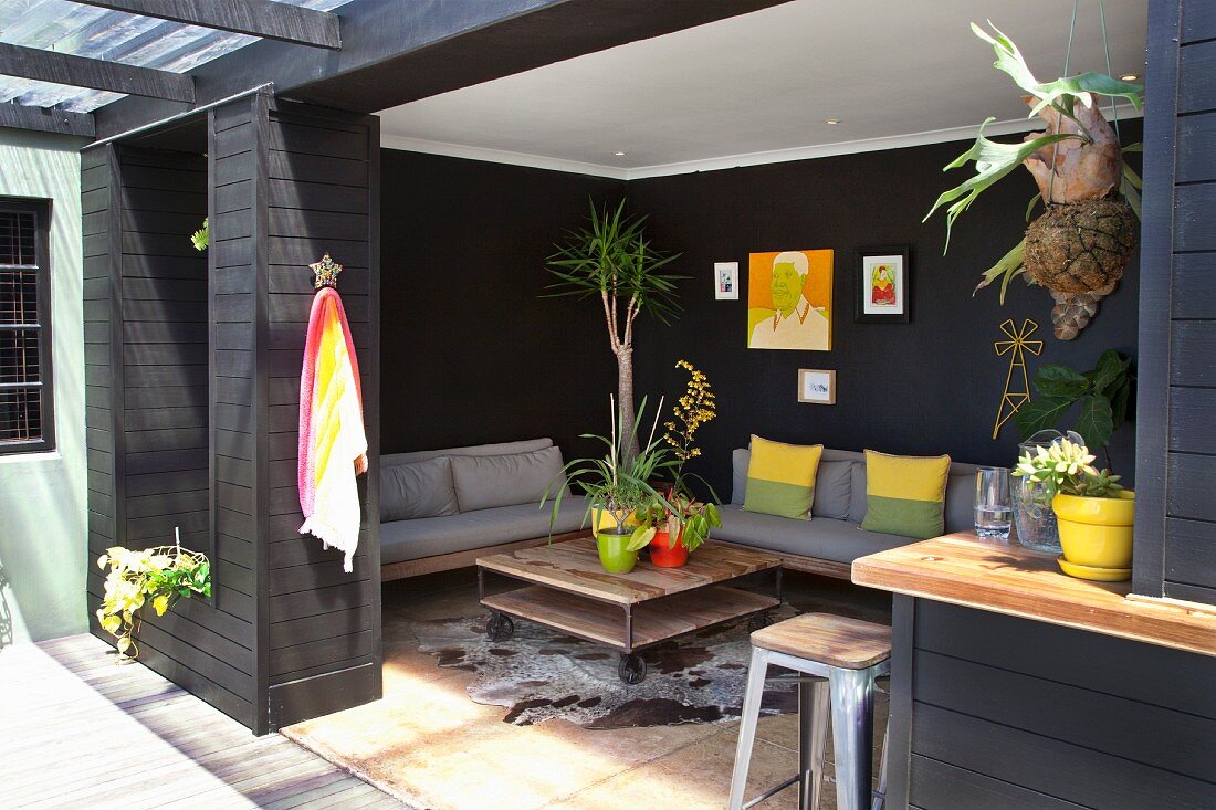 Comfortable lounge area in black-painted loggia; grey couches, bright scatter cushions and simple coffee table
