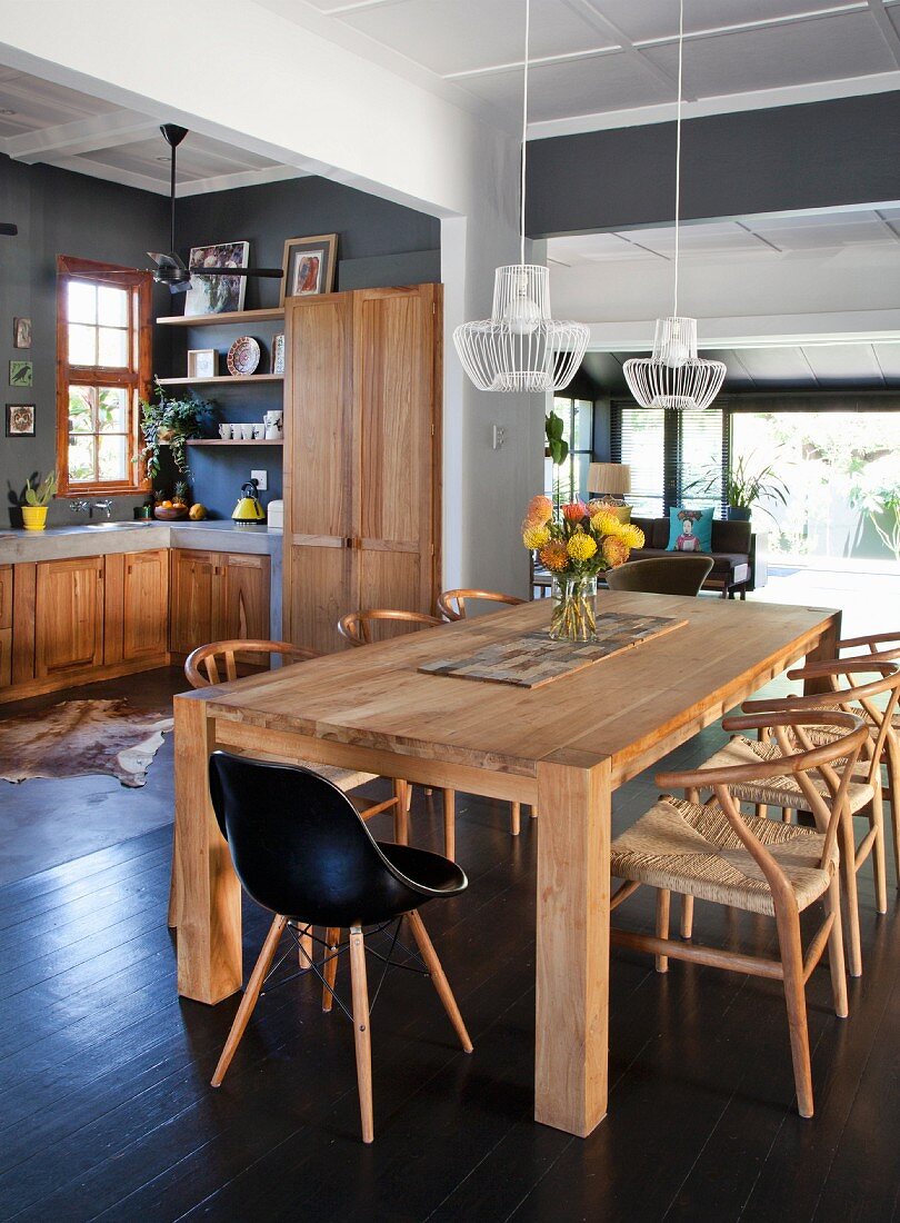 Black shell chair and classic, solid wood chairs around solid wood table in interior with open-plan kitchen