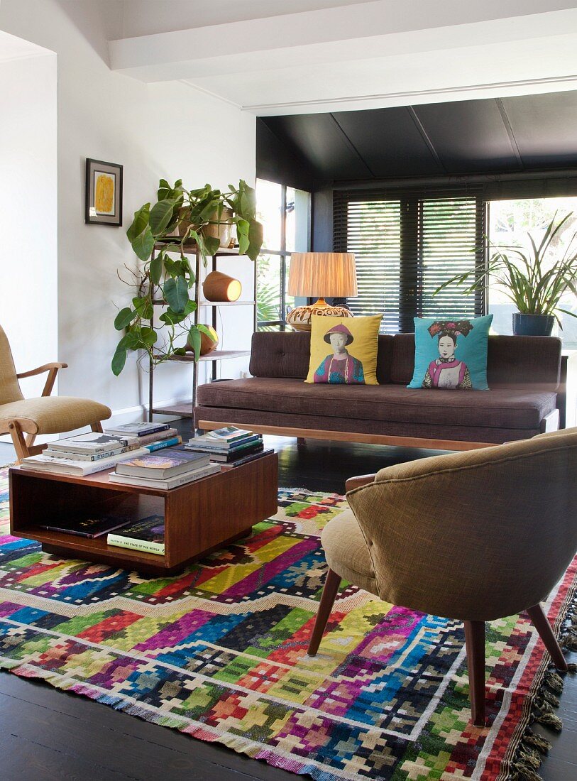 Sessel im Fiftiesstil und Coffeetable auf bunt gemustertem Teppich, Sitzbank mit braunen Polstern, in offenem Wohnraum