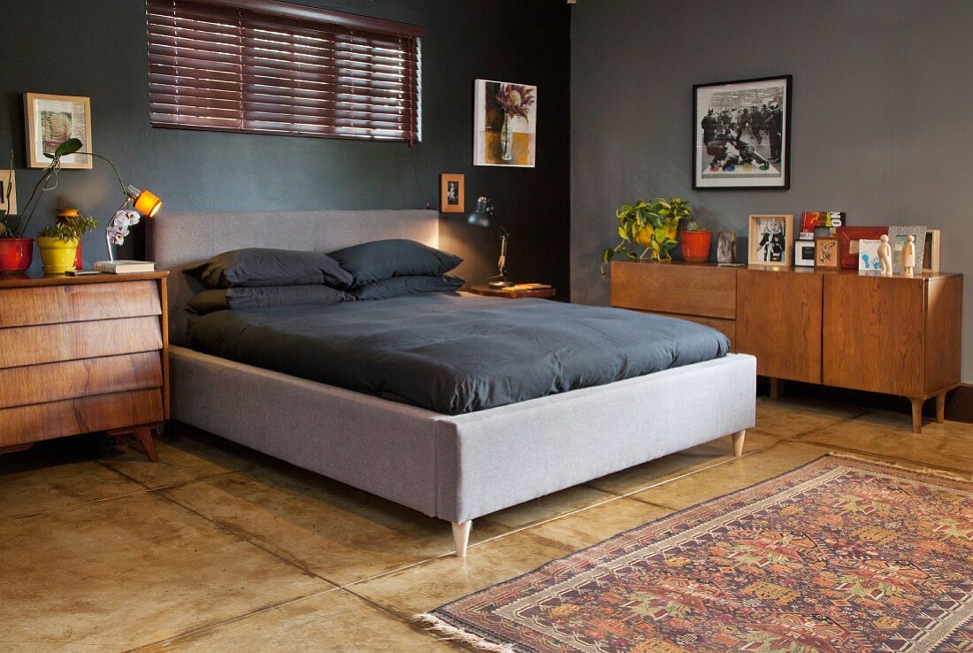 Master bedroom with double bed and black bed linen in dark-painted room with solid wooden sideboard