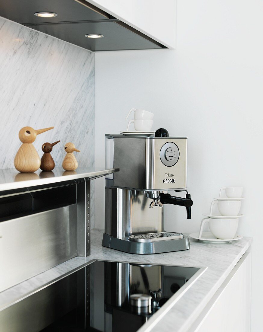 weiße Küche mit Marmor Rückwand und Arbeitsfläche - Edelstahl-Ablage, integriertes Kochfeld und Espressomaschine