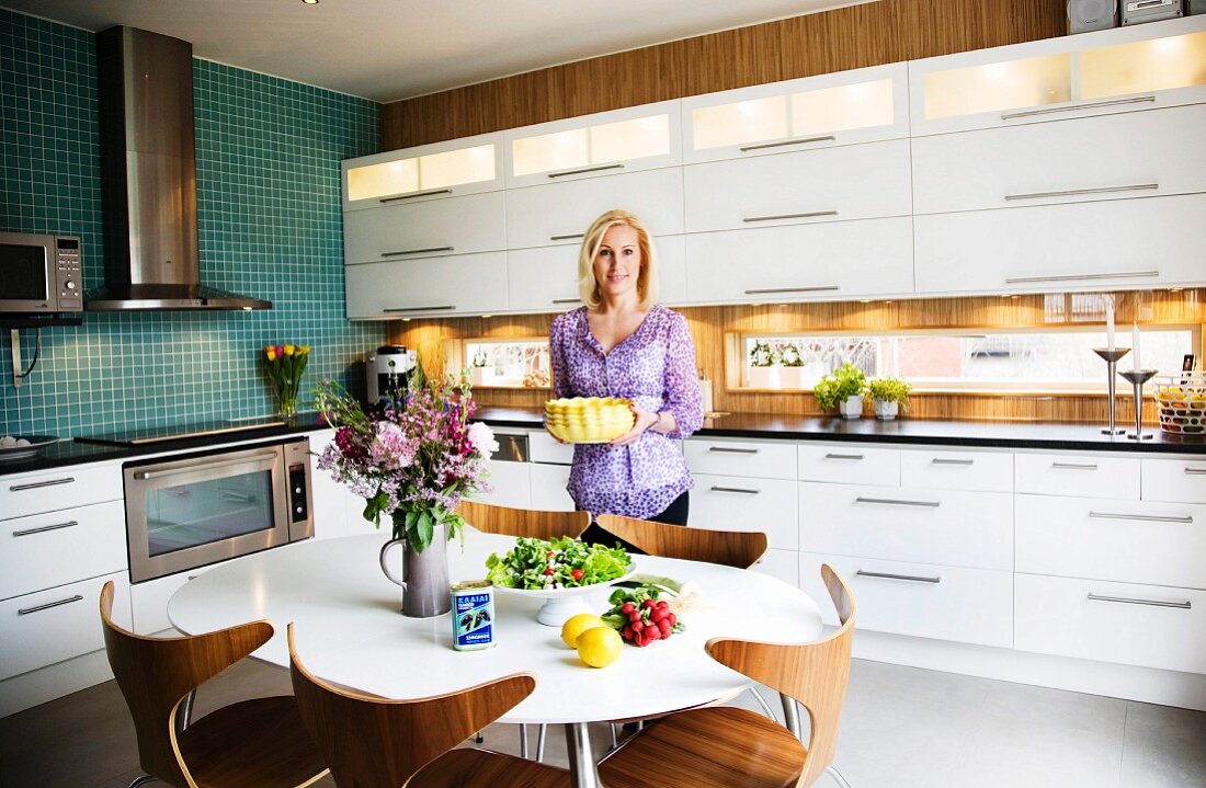 Einbauküche mit weissen Schrankfronten und teilweise Holzverkleidung an Wand, weisser Esstisch mit Schalenstühlen