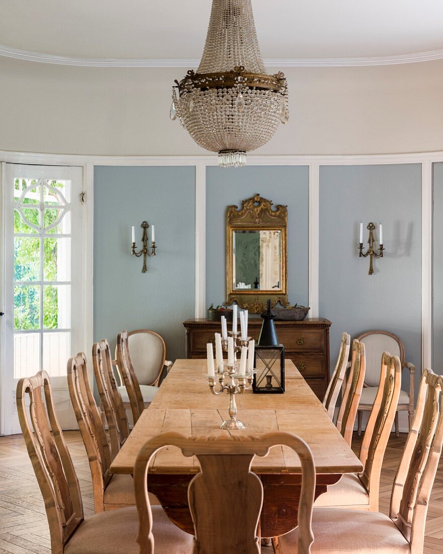 Langer rustikaler Holztisch und Stühle mit geschnitzter Rückenlehne in Esszimmer eines eleganten Landhauses, Kerzenständer auf Tisch und an Wand