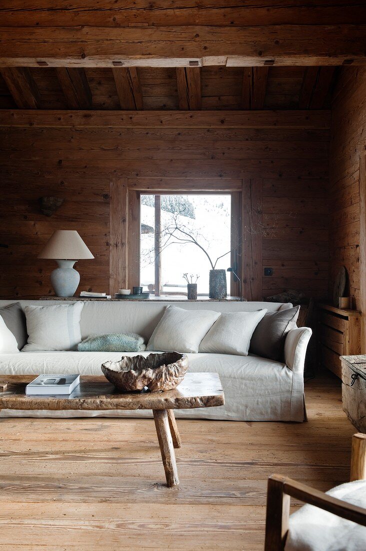 Helles Hussen-Sofa mit Kissen, davor rustikaler Holz Couchtisch im Wohnzimmer einer Hütte