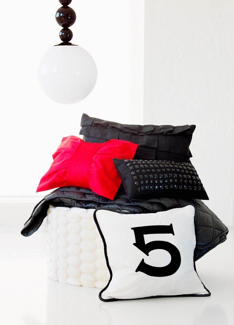 Inspired by Chanel; black and red cushions on white pouffe below spherical pendant lamp