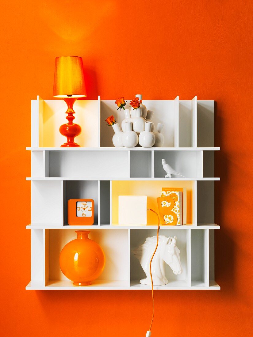 Weisses Regal mit Tischleuchten und Deko-Objekten an orangefarbener Wand