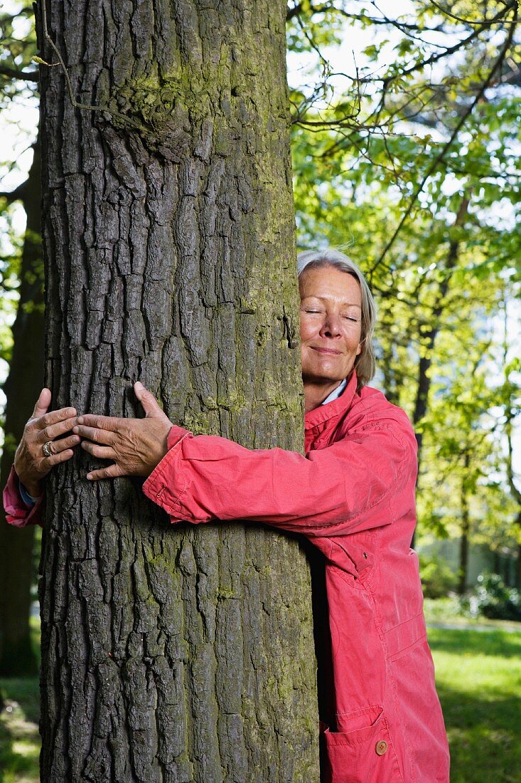 An older woman hugging a tree