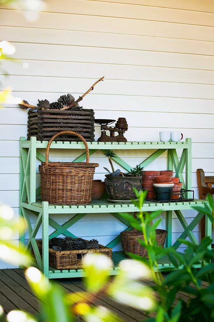 Lindgrünes Holzregal für Gartenutensilien vor weißer Bretterwand auf der Veranda