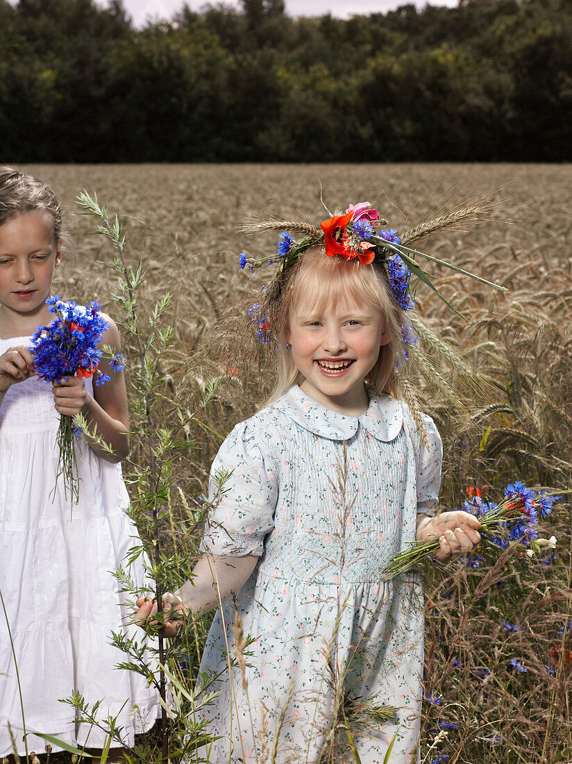 Zwei Mädchen im Kornfeld mit Blumenkranz im Haar und Kornblumenstrauss in Hand haltend