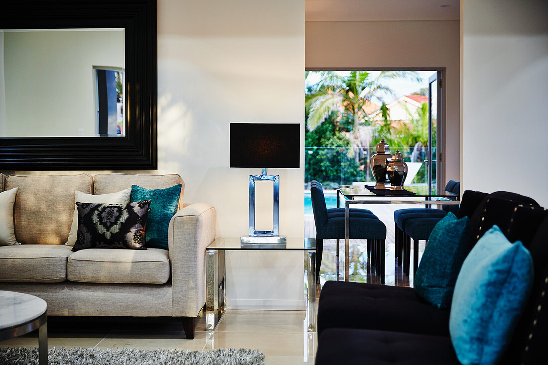 Modern living room with sofas, mirror on wall, metal table, rug and lamps on glass side tables