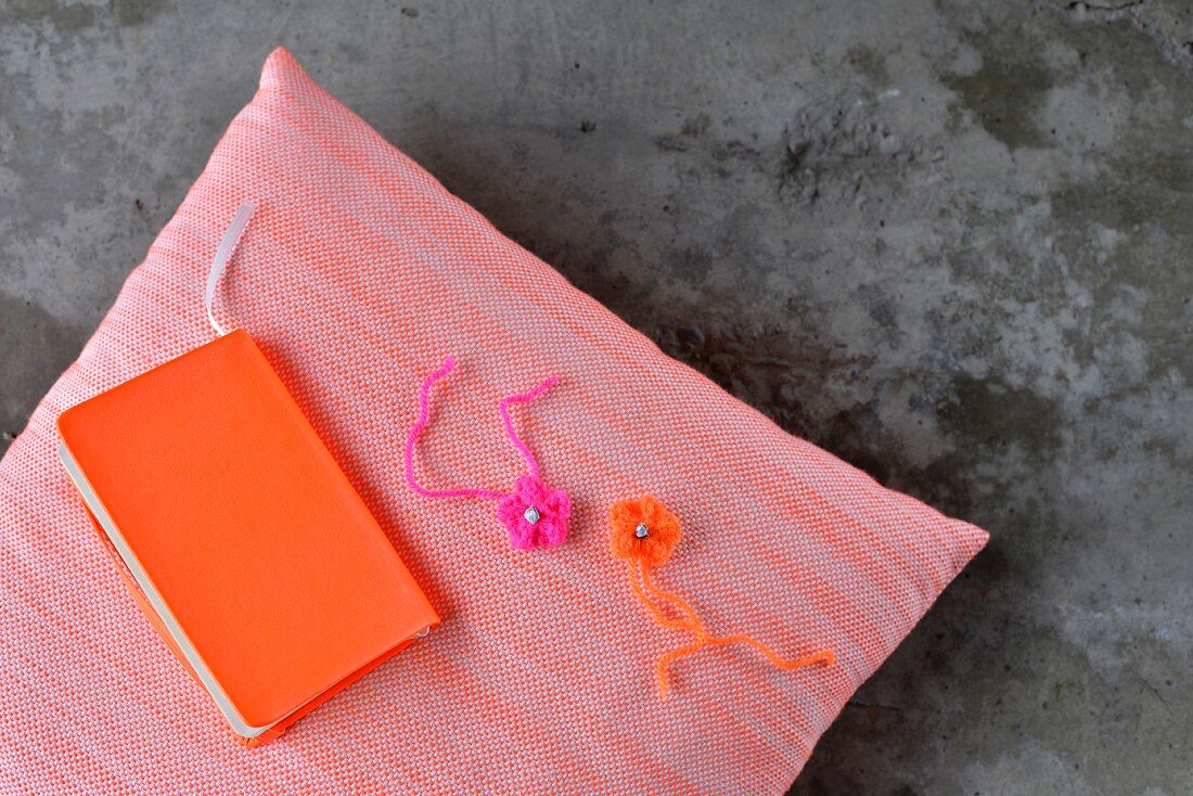 Hand-crafted book cover in neon orange and crocheted flowers on cushion