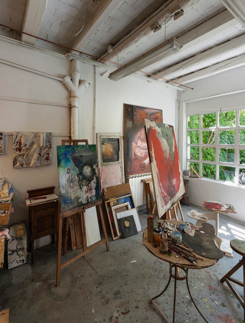 Artist's studio - painting utensils on side table and pictures on easels in rustic ambiance