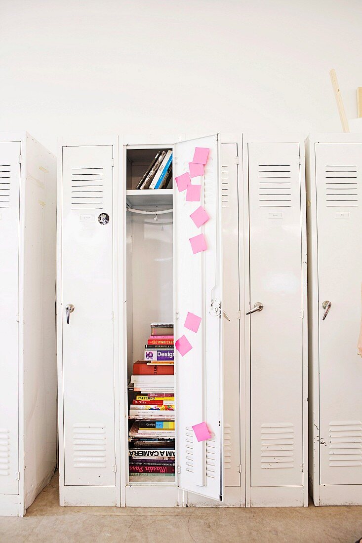 White locker cabinets with pink post-it notes inside one open door; stacked books stored inside