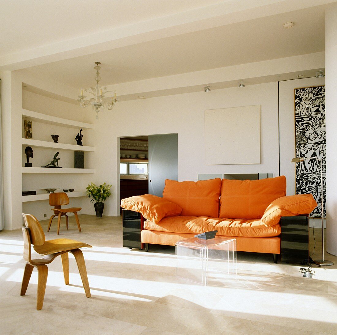 Sofa mit orangefarbener Polsterung und Couchtisch-Set aus Plexiglas in einem Wohnzimmer; im Vordergrund Designer-Stuhl aus Holz