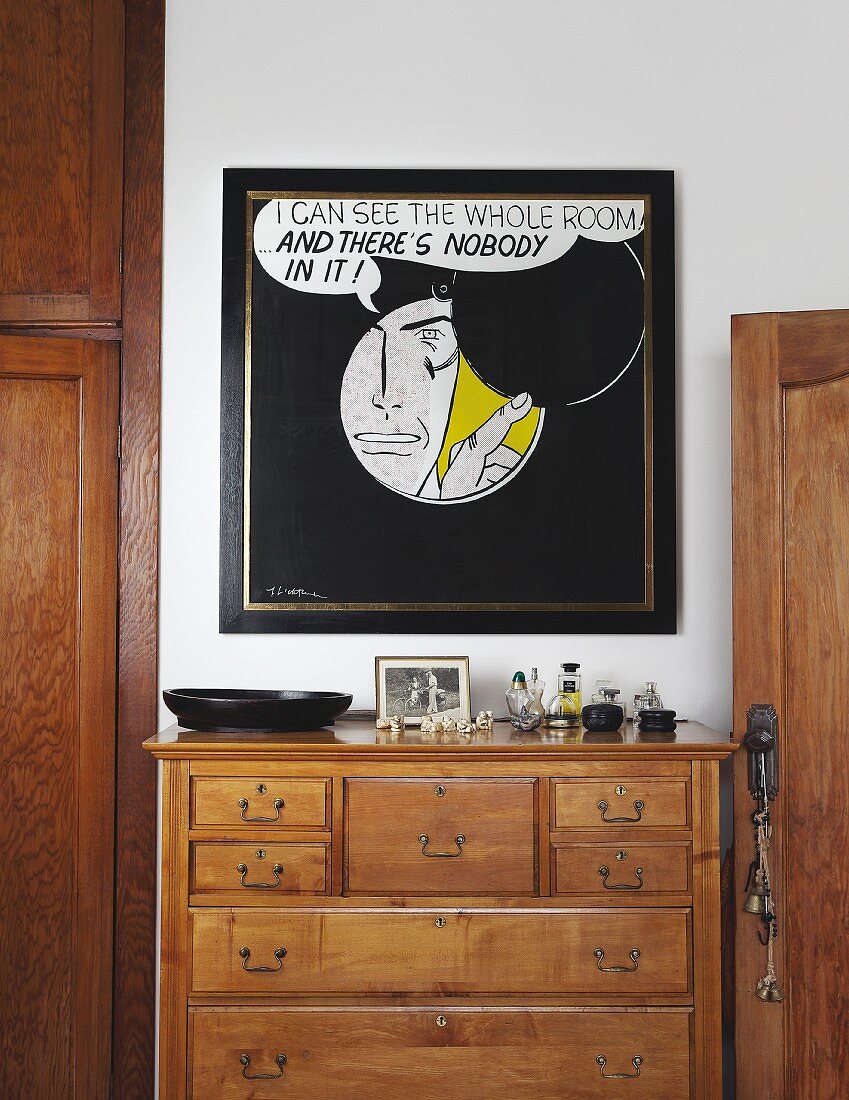 Wooden chest of drawers below framed, comic-style artwork