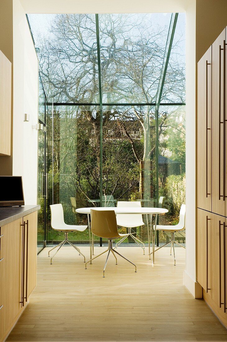 Blick durch offenen Küchenbereich auf Esstisch mit modernen Drehstühlen im verglasten Wintergarten mit Gartenblick
