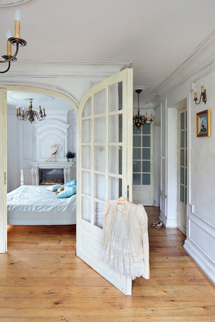 Open wing of double doors, view into bedroom in traditional apartment with rustic wooden floor