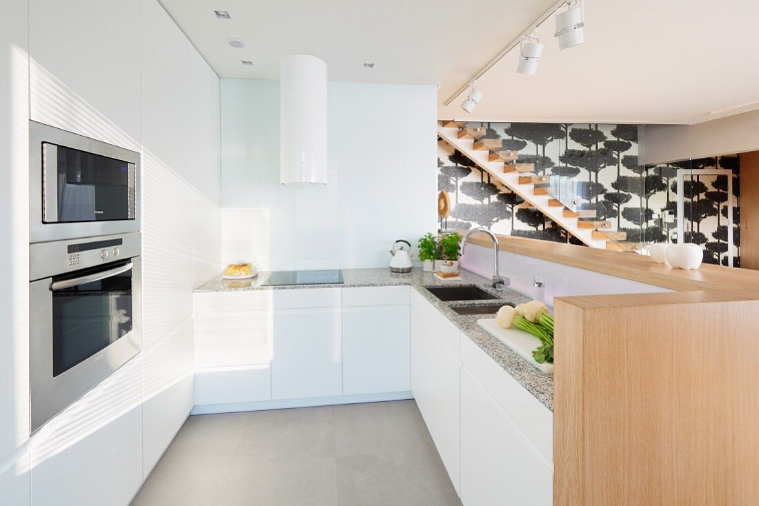 Minimalist, designer kitchen with white, flat-fronted cupboards, sink integrated into counter and fitted ovens in open-plan interior
