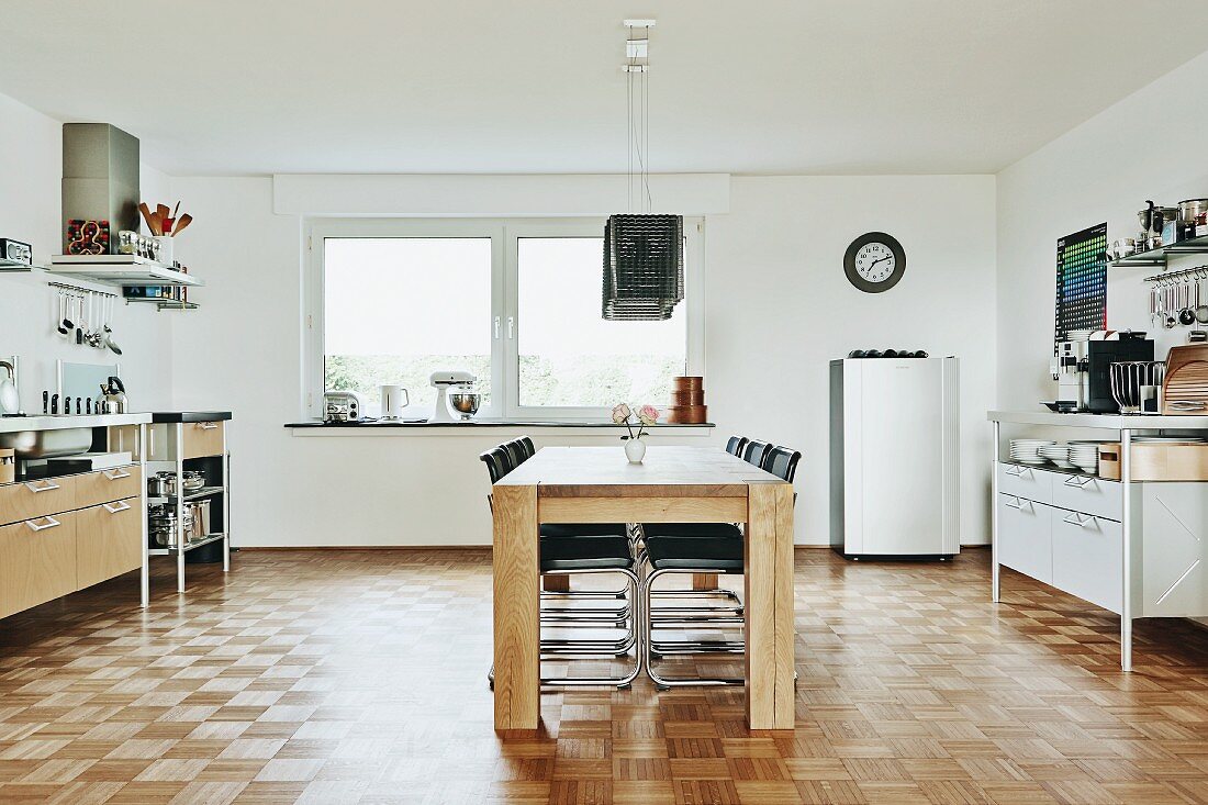 Dining area with wooden table and cantilever chairs and kitchen counter elements along side walls in minimalist kitchen with mosaic parquet floor