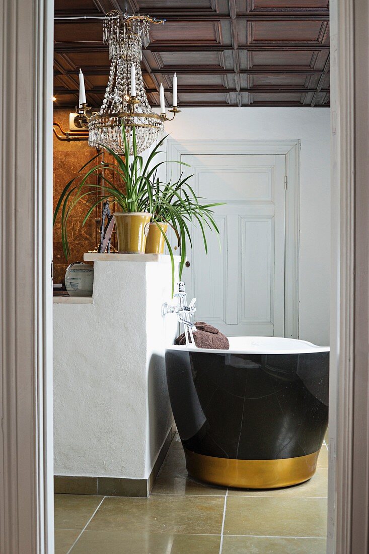Blick durch offene Tür auf freistehende Badewanne mit schwarzer Aussenwand und goldenem Streifen