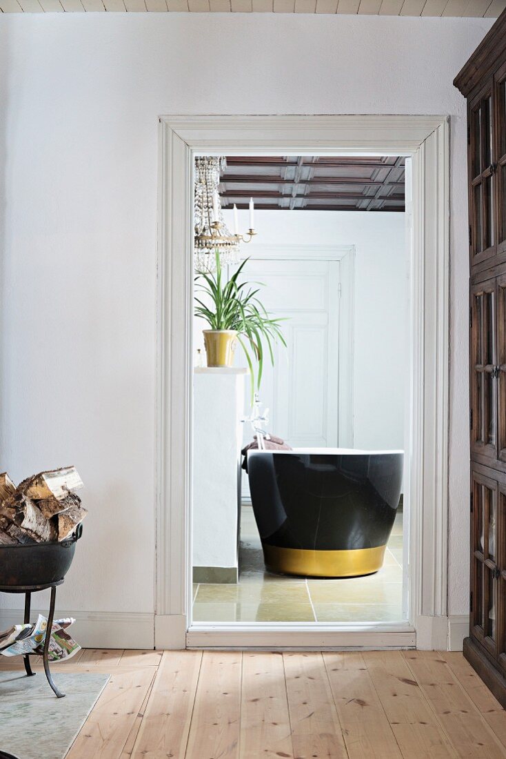 Blick durch offene Tür ins Bad auf freistehende Badewanne in Schwarz mit goldenem Streifen