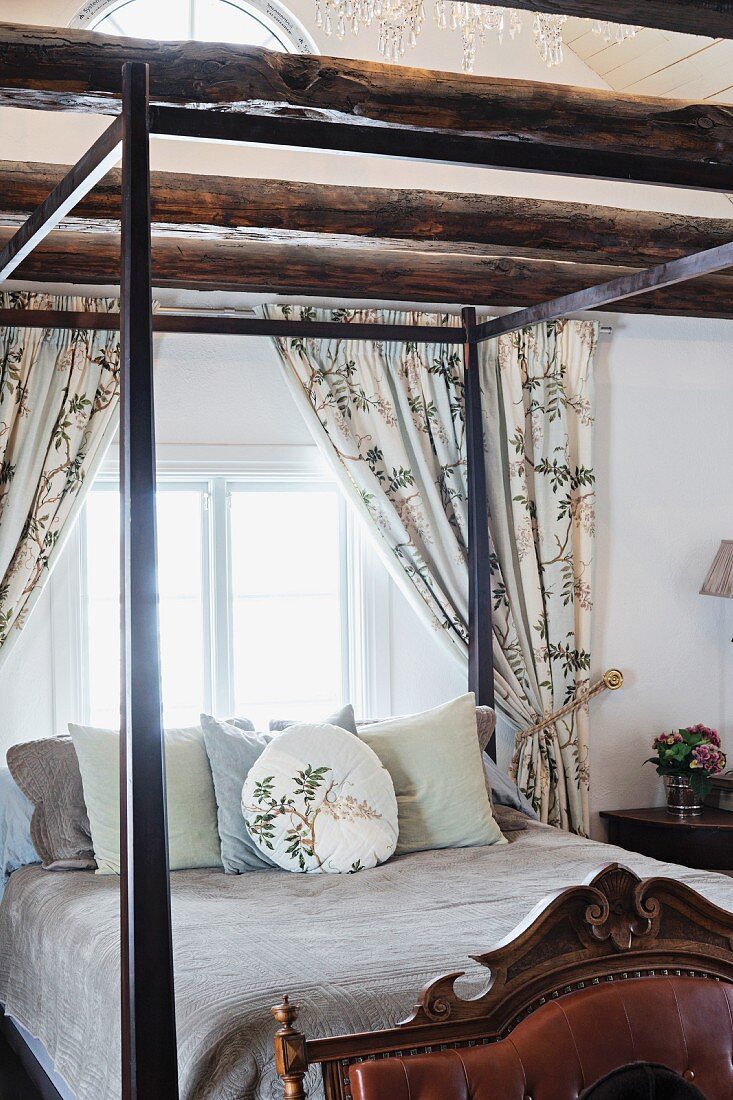 Bett mit Himmelgestell aus dunklem Holz, Kissenstapel, vor Fenster in Schlafzimmer mit Holzbalkendecke