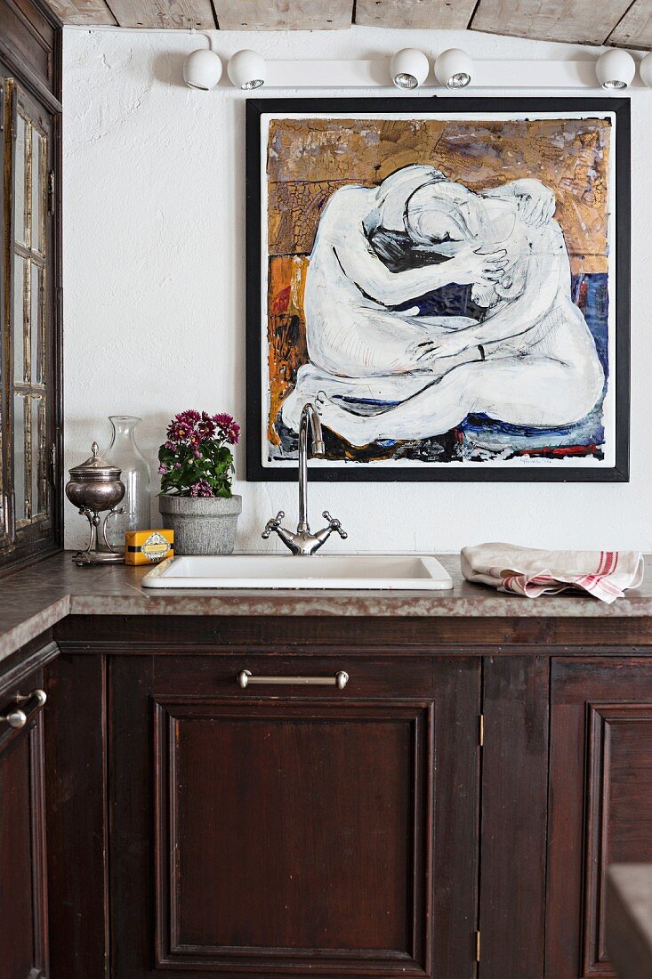 Küchenzeile mit Unterschrank aus dunklem Holz und Spülbecken mit Vintage Armatur, vor Wand mit modernem Gemälde