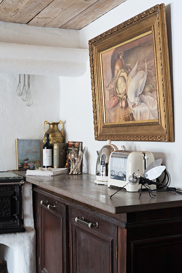 Halbhoher Küchenschrank aus dunklem Holz, darauf Retro Elektrogeräte, vor Wand mit Bild in Goldrahmen