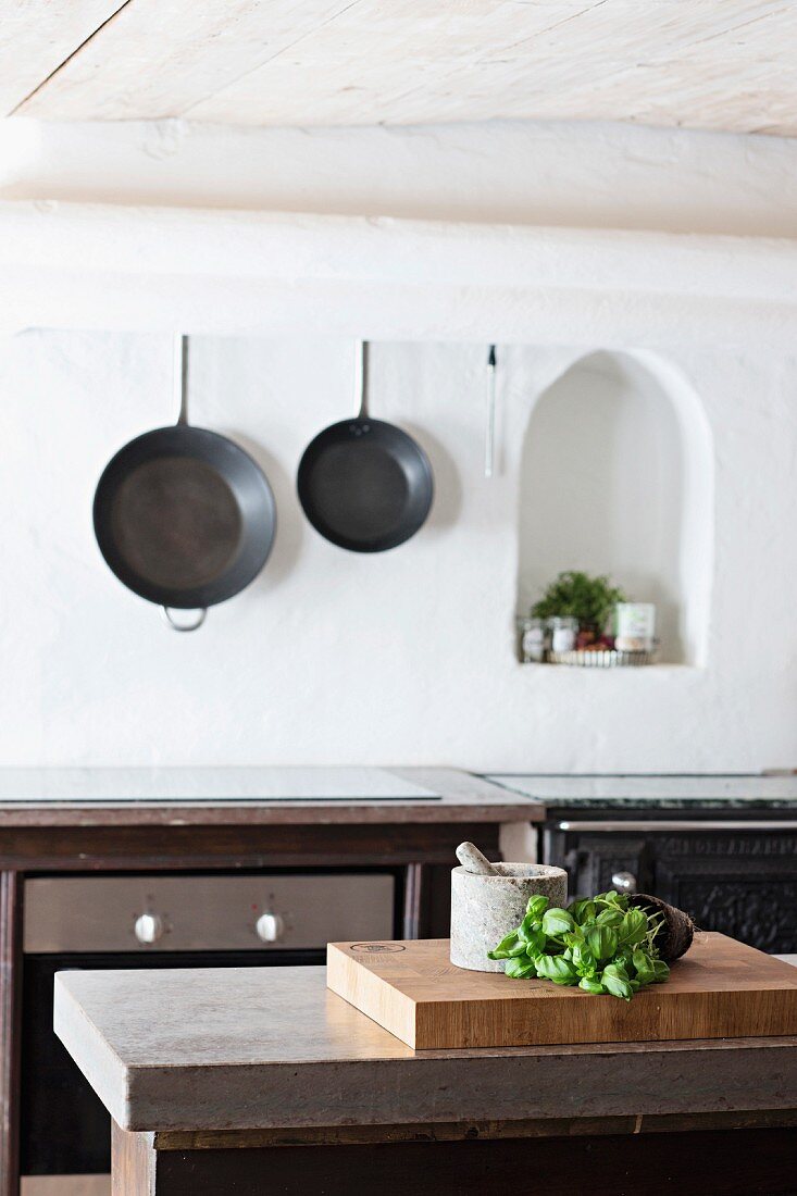 Theke mit Küchenutensilien, an Wand gusseiserne Pfannen neben Nische mit Rundbogen