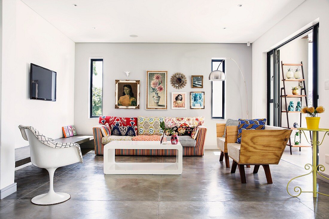 Stilmix in minimalistischem Wohnraum mit Estrichboden, weisser Retro Kunststoff Stuhl und Sessel mit Holzschale um modernen Couchtisch, dahinter buntes Sofa