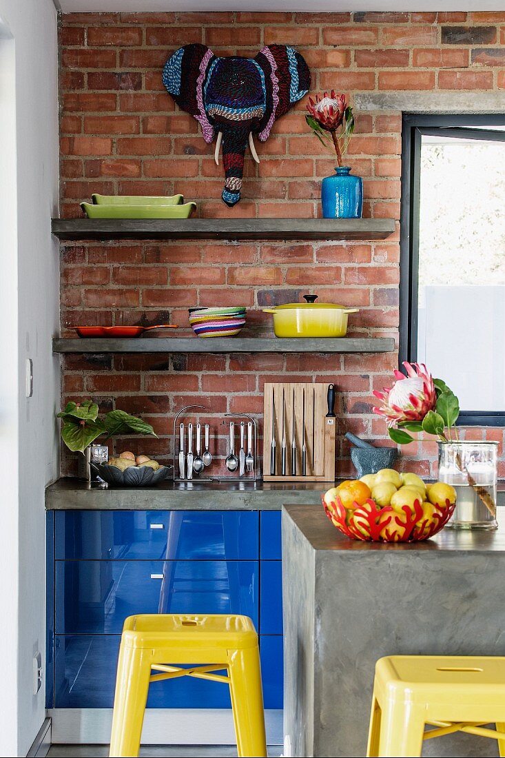 Detail of concrete counter and retro, yellow bar stools in front of kitchen counter with blue fronts against brick wall