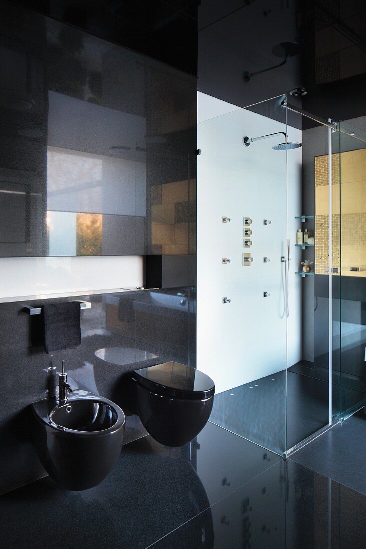 Schwarz gefliestes Designerbad mit schwarzen Sanitärobjekten, neben verglaster, bodenebener Dusche