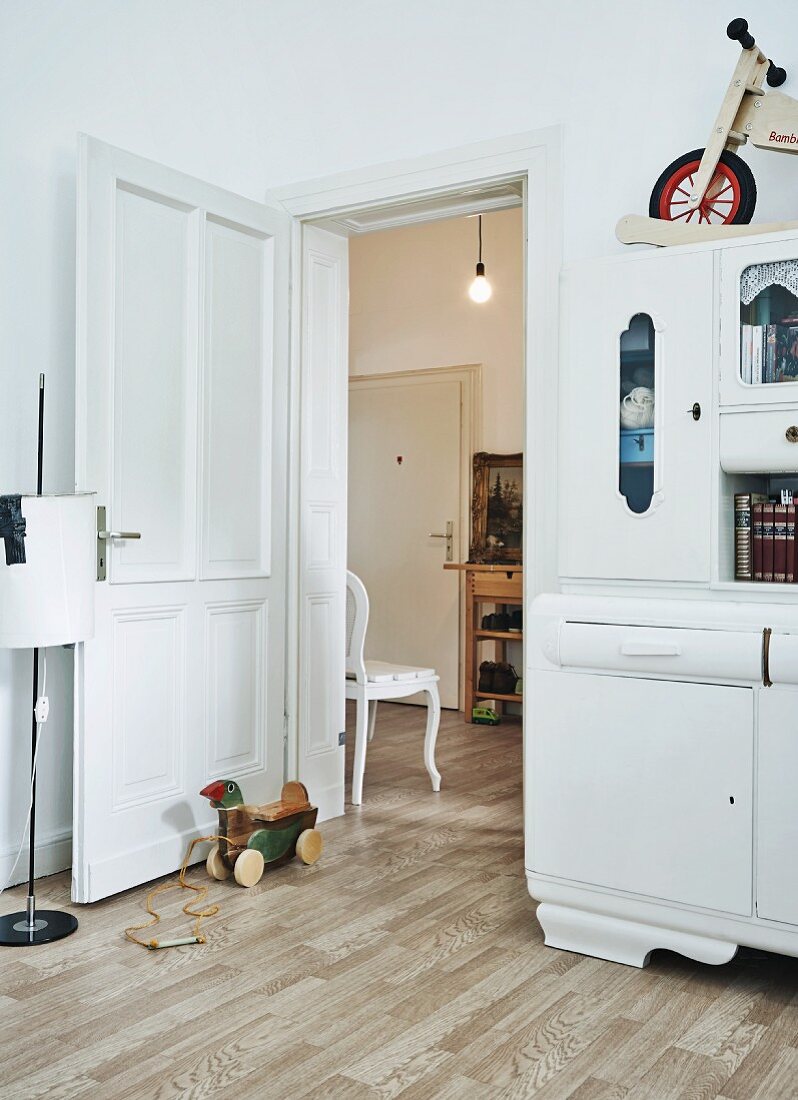 Blick aus der Wohnküche mit geerbtem, weiss lackiertem Küchenbuffet in die geräumige Diele einer Altbauwohnung