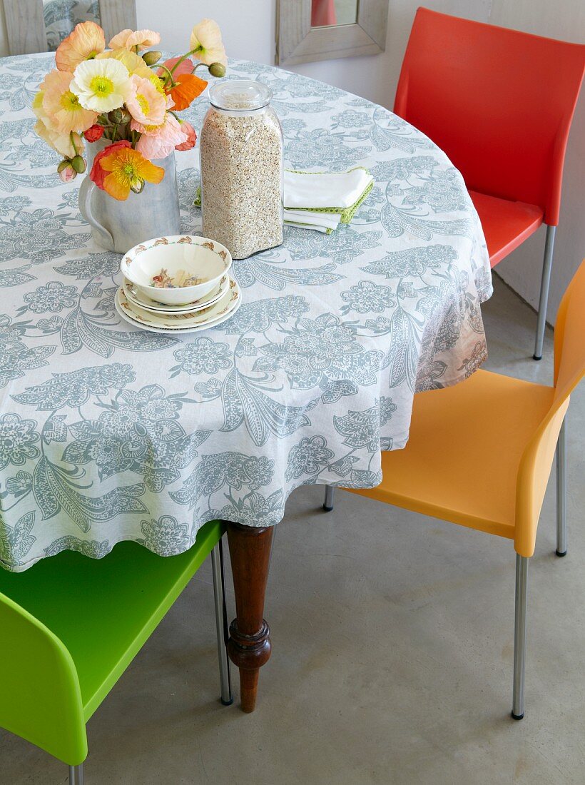 Runder Esstisch mit Blumenmuster-Tischdecke und modernen farbigen Stühlen