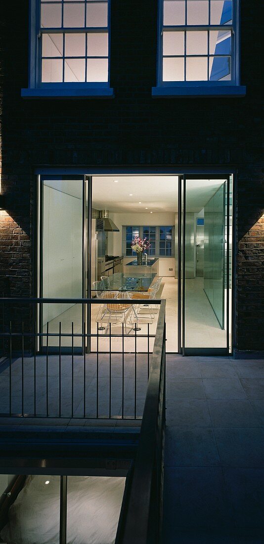 Wohnhaus in Abendstimmung mit offenen Terrassentüren und Blick in beleuchtetes Esszimmer