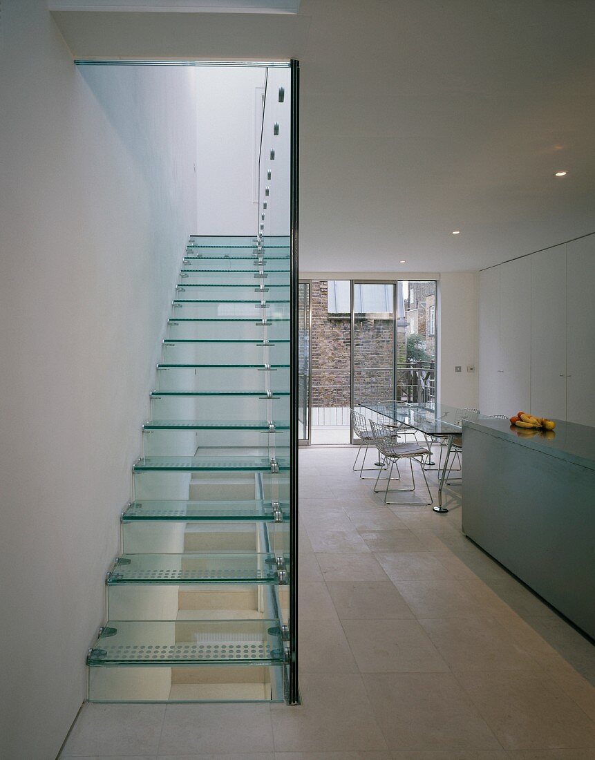View of the glass stairs of a stairway and glass dividing wall in an open designer kitchen with dining area