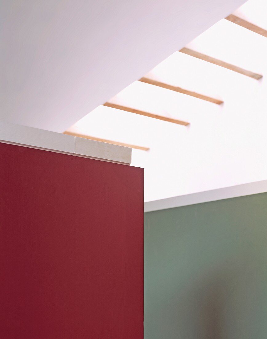 Corner of wall panel painted in a shade of red in front of a gray wall under a skylight in contemporary architecture